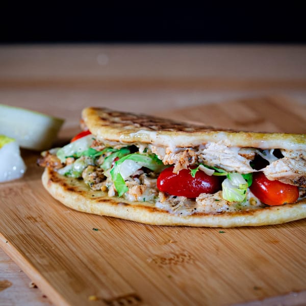 Appletree Deli's chicken pita sandwich with lettuce, tomatoes, and cheese on a wooden board.