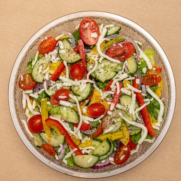 Overhead view of a colorful garden salad with tomatoes, cucumbers, bell peppers, and shredded cheese.