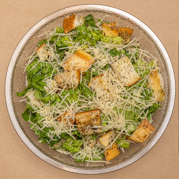 Caesar salad in a glass bowl, topped with shredded Parmesan cheese, croutons, and black pepper.