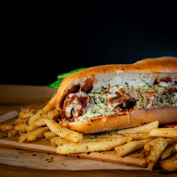 A meatball sub sandwich with melted cheese and parsley, surrounded by seasoned french fries.