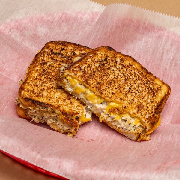 Two halves of a grilled cheese sandwich with tuna salad, served in a red basket with pink paper.