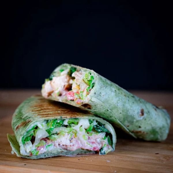 Two halves of a grilled green wrap, filled with chicken, lettuce, and creamy sauce, on a wooden board.