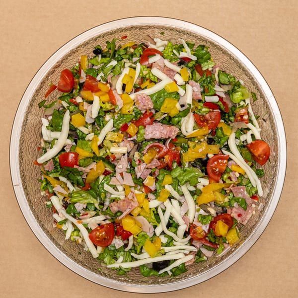 Chopped salad with lettuce, tomatoes, bell peppers, cheese, and deli meat in a glass bowl.