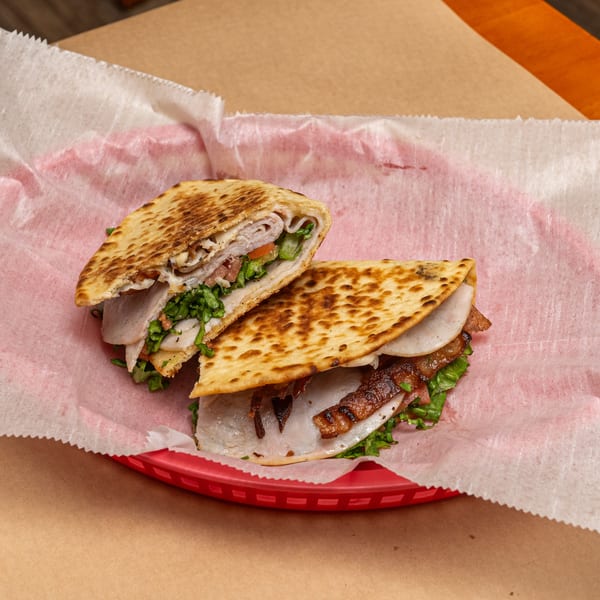Two halves of a grilled Appletree Deli sandwich with turkey, bacon, and lettuce in a red basket.